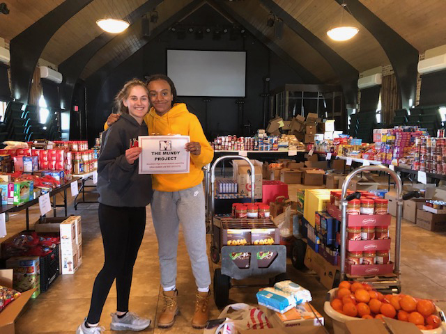 Two student volunteers hugging each other in front of all the food being provided