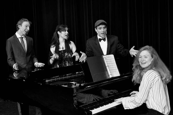 Cast members rehearse around the piano.