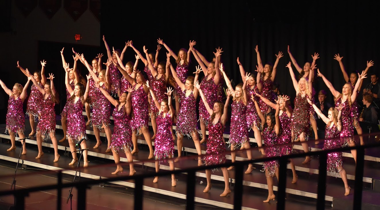 The all-female group performs in sequined dresses