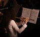 Photo looking over a flute player's back showing the flute and music