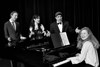 Cast members rehearse around the piano.