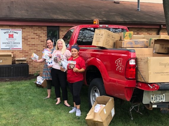 The Osco pharmacy manager and two school officials stand next to a red pickup truck loaded with masks and hand sanitizer for Mundelein schools.