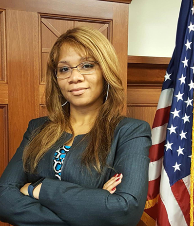 Photo of Zaneta standing in a courtroom with the US Flag to her side