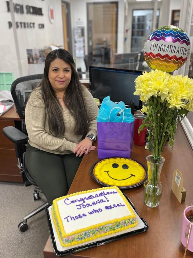 Joanna Rodriguez sits near flowers and a cake in honor of her award.